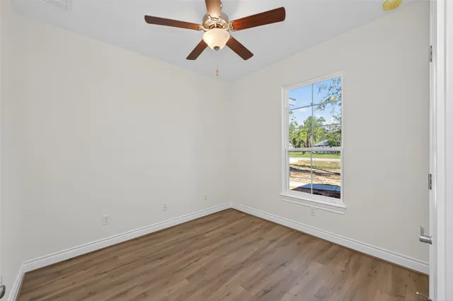 an empty room with wooden floor chandelier fan and windows