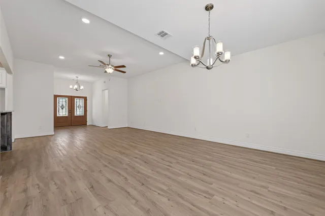 a view of an empty room with wooden floor and a ceiling fan