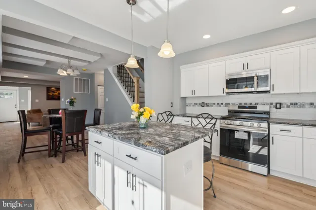 a kitchen with stainless steel appliances granite countertop a stove top oven a sink dishwasher a dining table and chairs with wooden floor