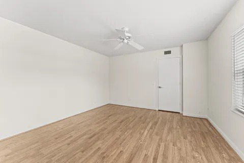 an empty room with wooden floor ceiling fan and windows