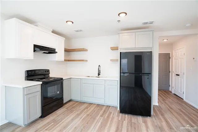 a kitchen with stainless steel appliances a sink dishwasher a refrigerator and a stove with wooden floors