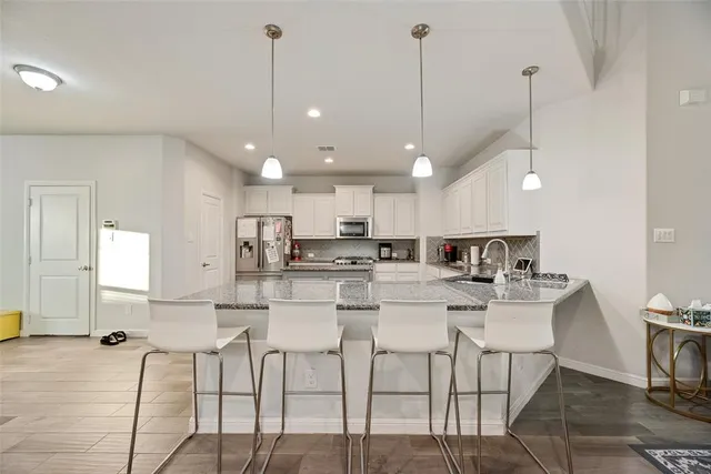a kitchen with stainless steel appliances kitchen island granite countertop a dining table chairs and a refrigerator