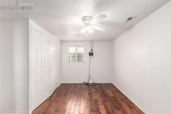 an empty room with wooden floor chandelier fan and windows