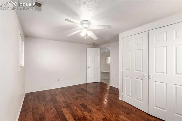an empty room with wooden floor closet fan and windows