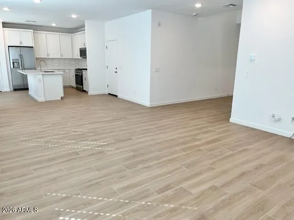 an empty room with wooden floor and kitchen view