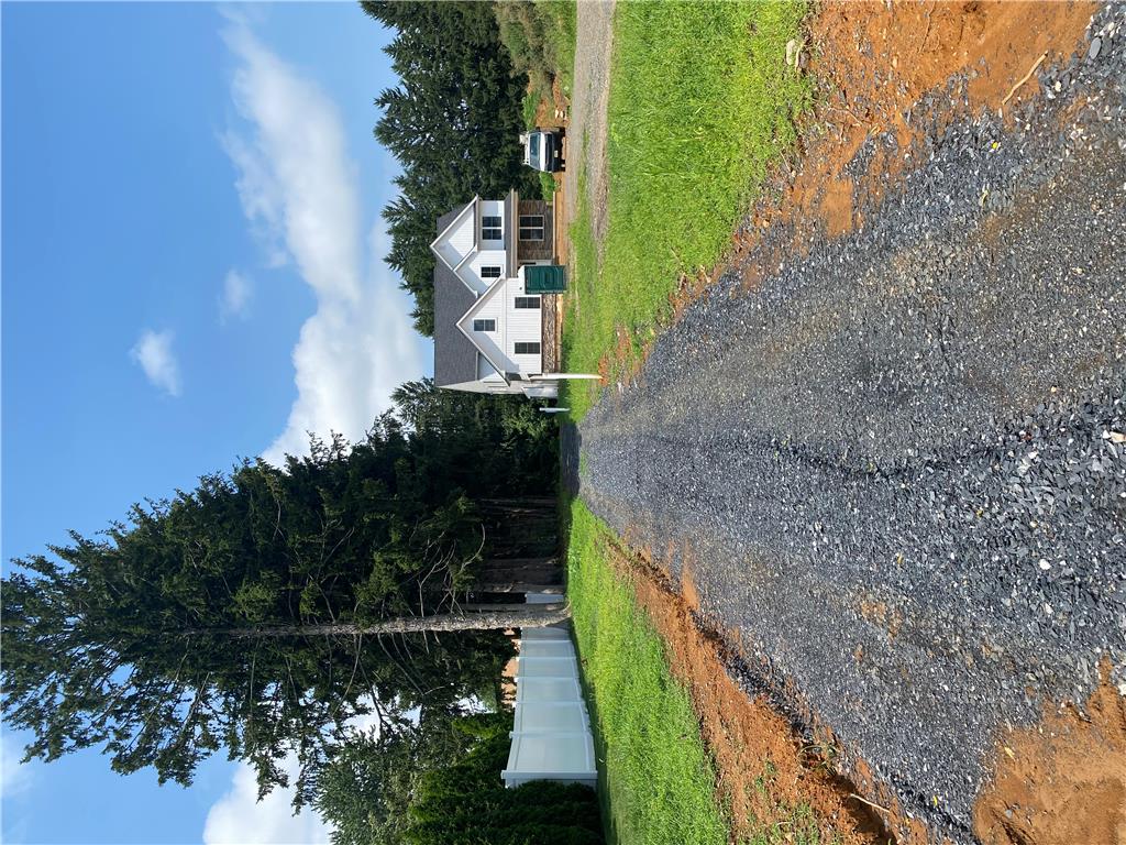 A newly graveled driveway leads to a charming residence nestled amidst verdant trees.
