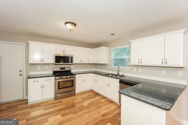 a kitchen with granite countertop a sink stainless steel appliances and white cabinets