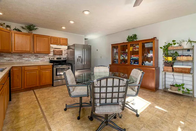 a kitchen with stainless steel appliances kitchen island granite countertop a dining table chairs and a refrigerator