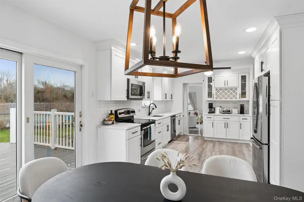 a kitchen with stainless steel appliances kitchen island granite countertop a refrigerator a stove a sink and white cabinets with wooden floor