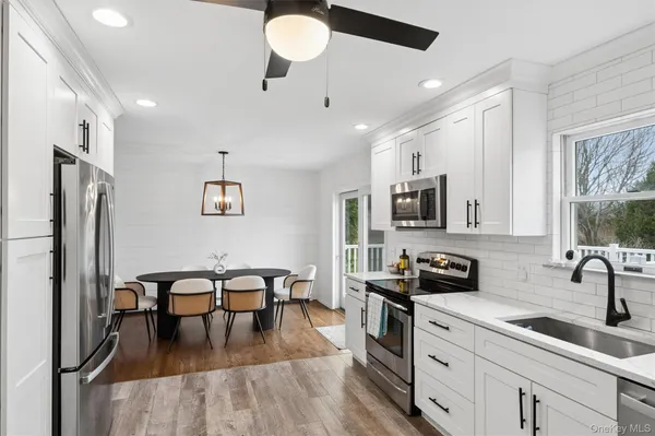 a kitchen with stainless steel appliances granite countertop a refrigerator a sink dishwasher a stove and white cabinets with wooden floor