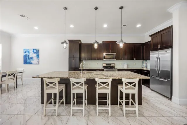a kitchen with stainless steel appliances granite countertop a sink a stove a refrigerator and chairs