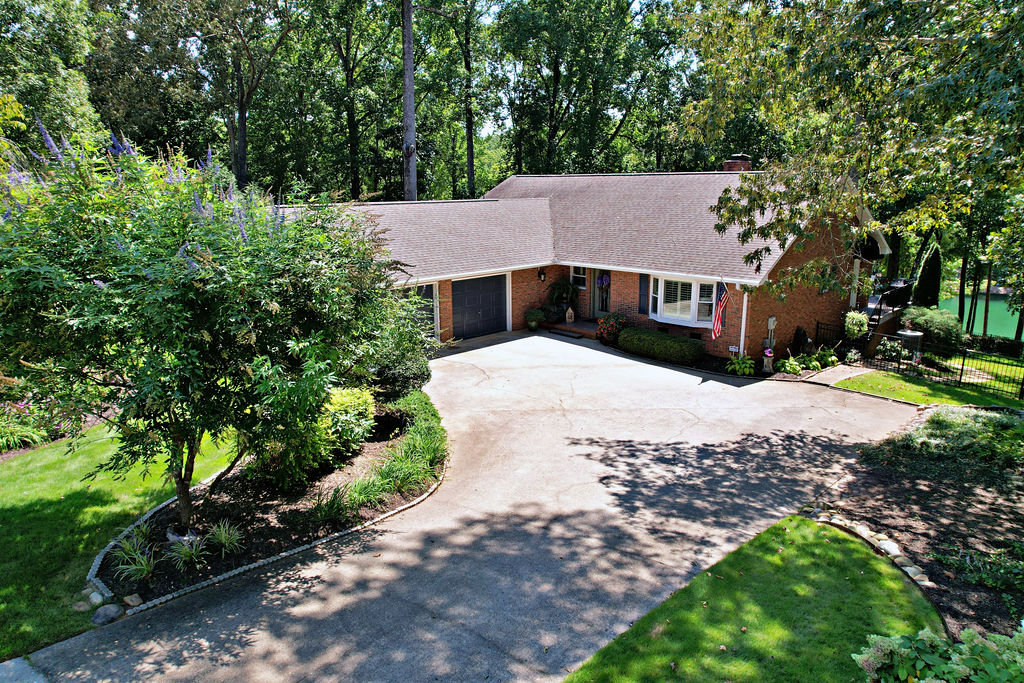 Mature trees frame a classic brick exterior with an attached garage and a concrete driveway.