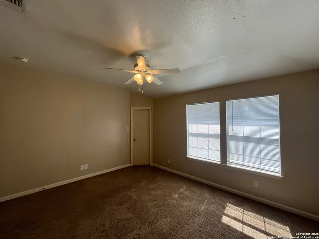 an empty room with a chandelier fan and windows