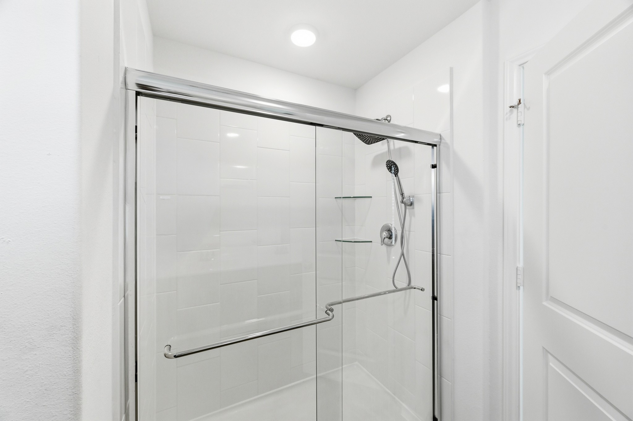 23427 Weir Box Road Hockley, TX 77447 - Photo 14 of 32 A closer look inside the primary bathroom's walk-in shower, featuring crisp white tiling, a contemporary sliding glass door, and integrated corner shelving.