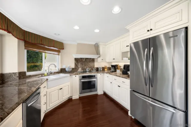 a kitchen with stainless steel appliances granite countertop a refrigerator a sink dishwasher a stove and white countertops with wooden floor