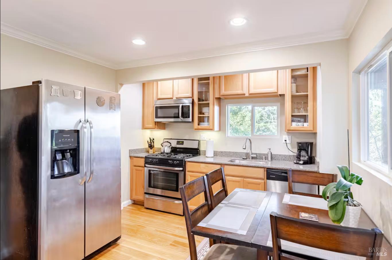 a kitchen with stainless steel appliances granite countertop a refrigerator a stove a sink a dining table and chairs with wooden floor