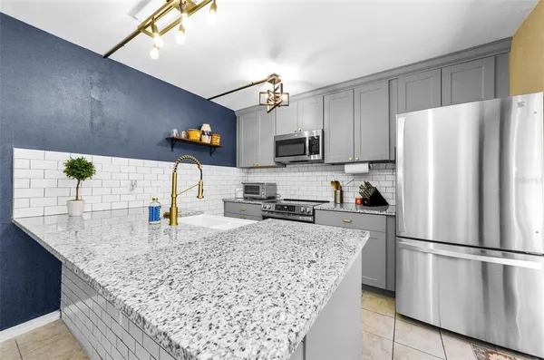 a kitchen with stainless steel appliances granite countertop a refrigerator a stove a sink a microwave a refrigerator and white cabinets with wooden floor