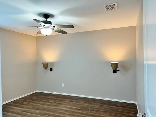 an empty room with wooden floor fan and windows