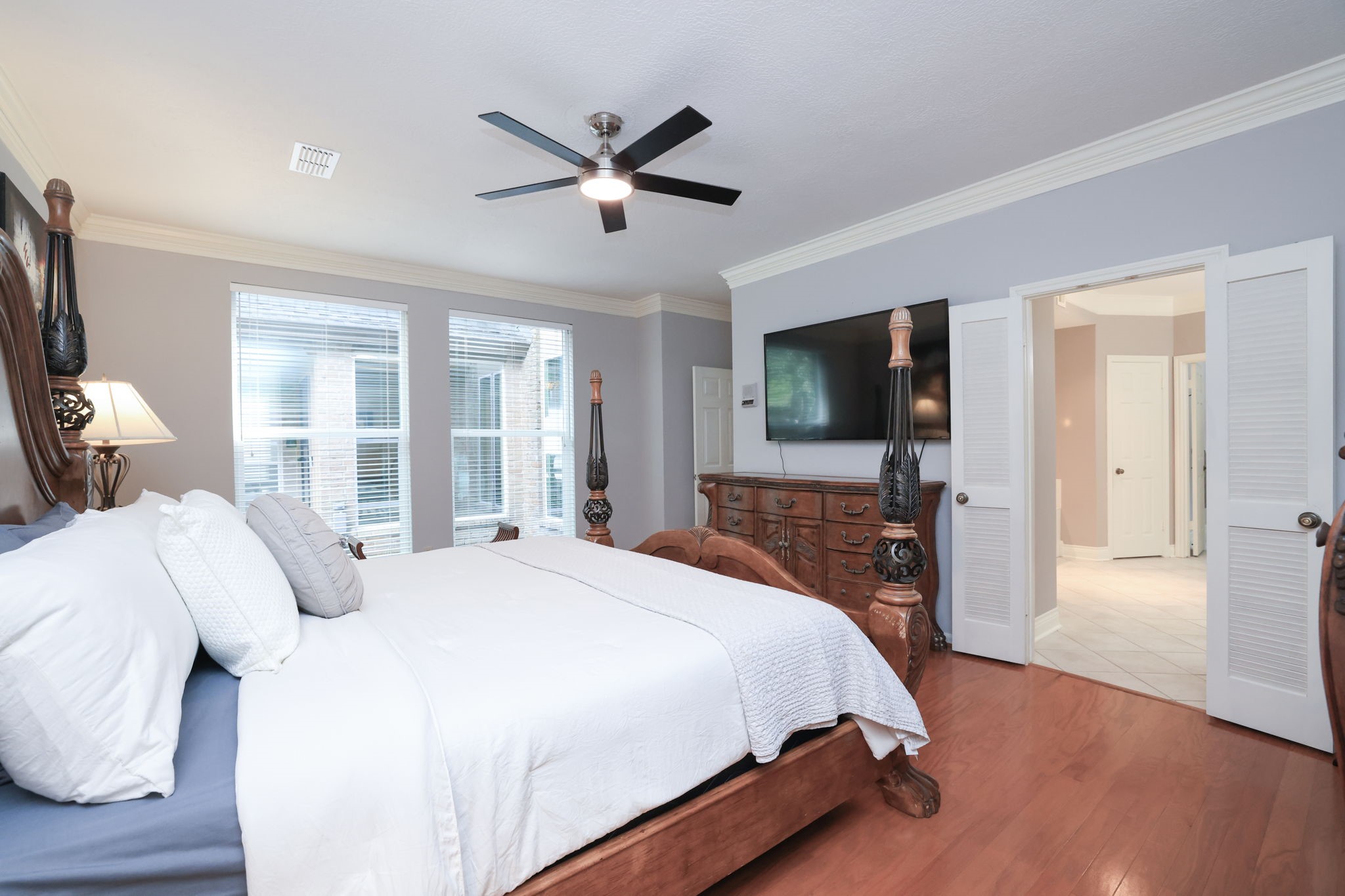 16123 Chasemore Drive Spring, TX 77379 - Photo 27 of 50 Spacious, elegant primary bedroom with hardwood floors, large windows for natural light, and an ensuite bathroom with white double doors.