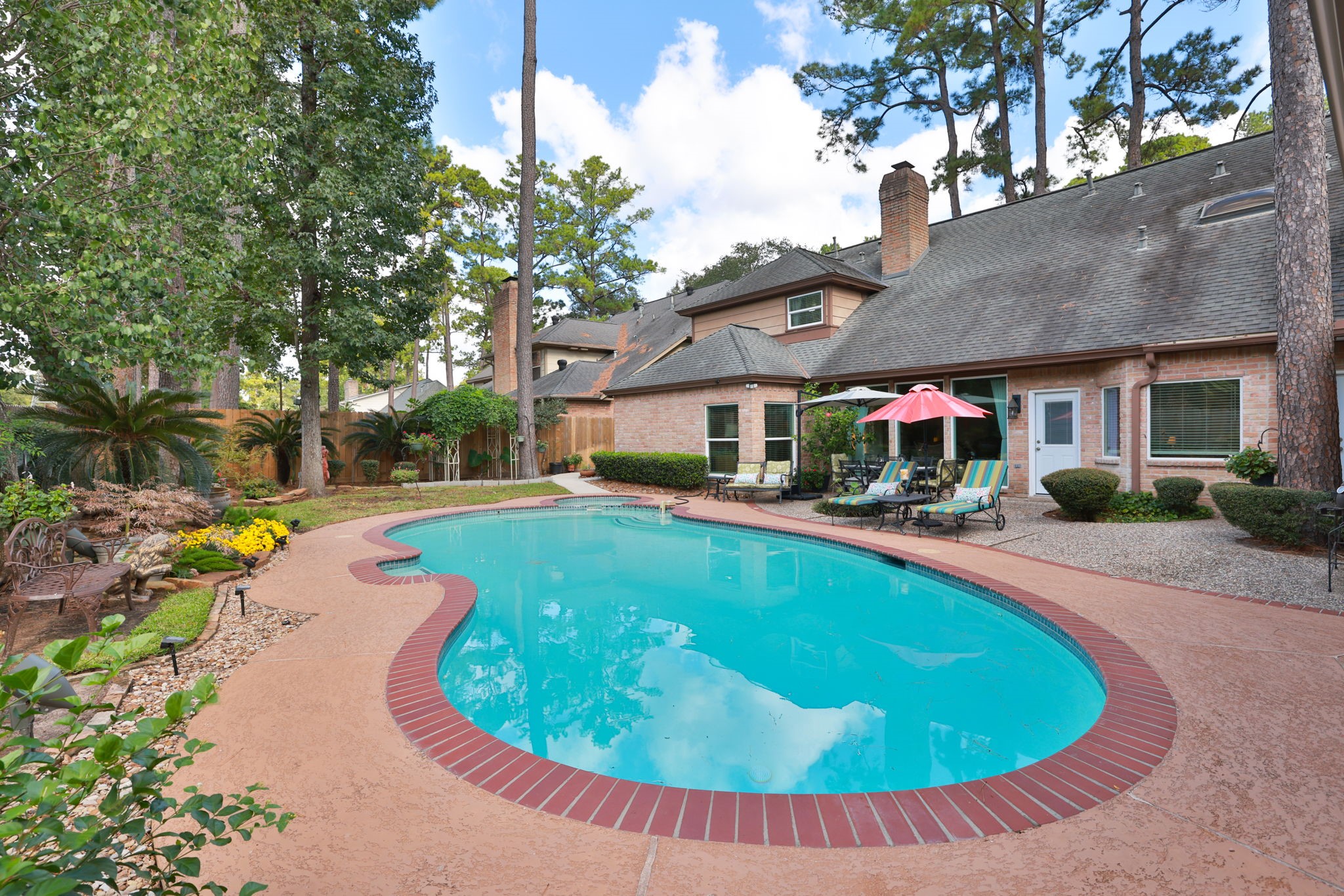 16123 Chasemore Drive Spring, TX 77379 - Photo 43 of 50 This backyard features a beautifully landscaped area with pool and spa surrounded by trees and lush greenery.