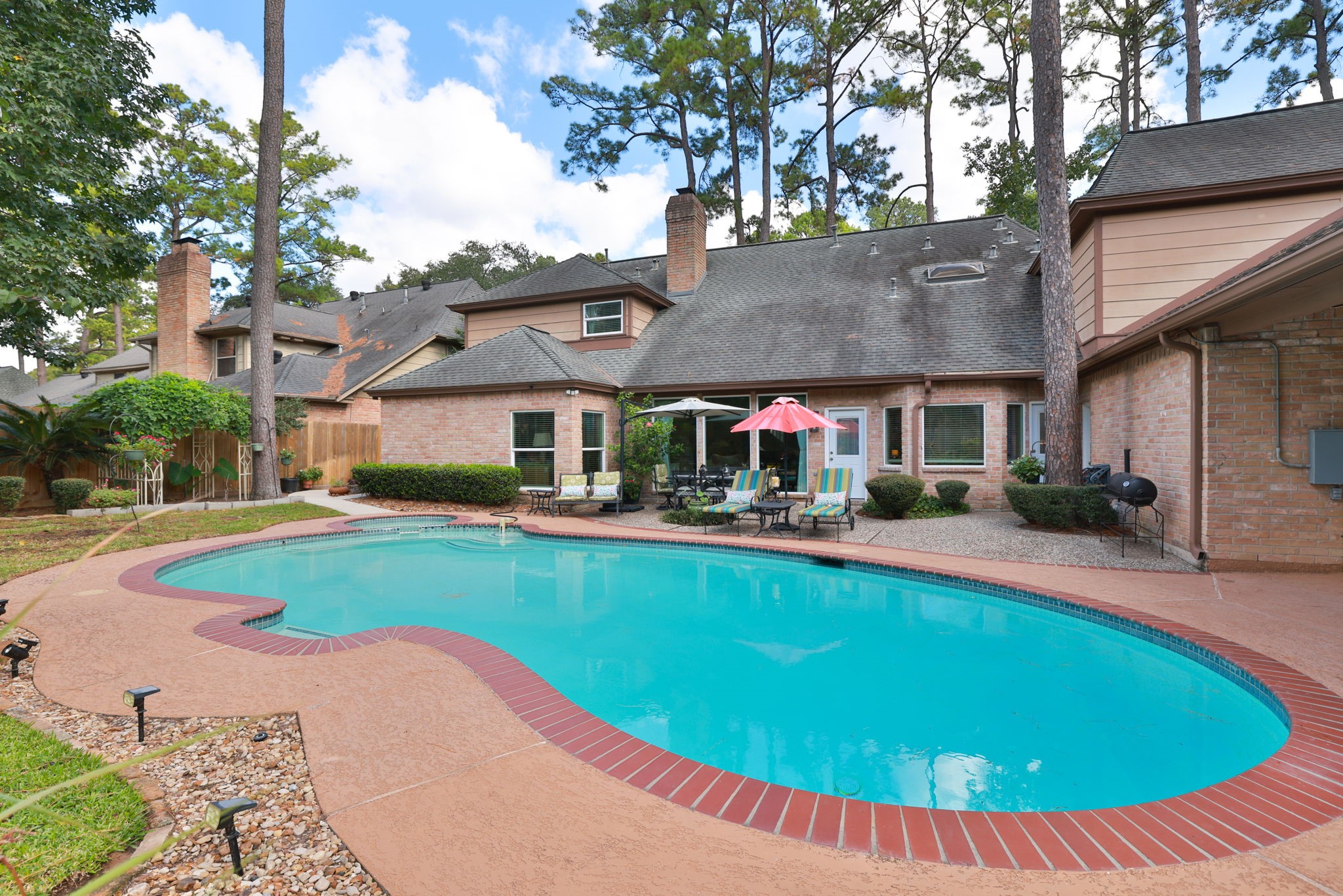 16123 Chasemore Drive Spring, TX 77379 - Photo 44 of 50 This inviting backyard features a spacious inground pool with a surrounding patio, perfect for outdoor relaxation and entertainment. The brick exterior of the home complements the natural setting, offering a private oasis amidst tall trees.