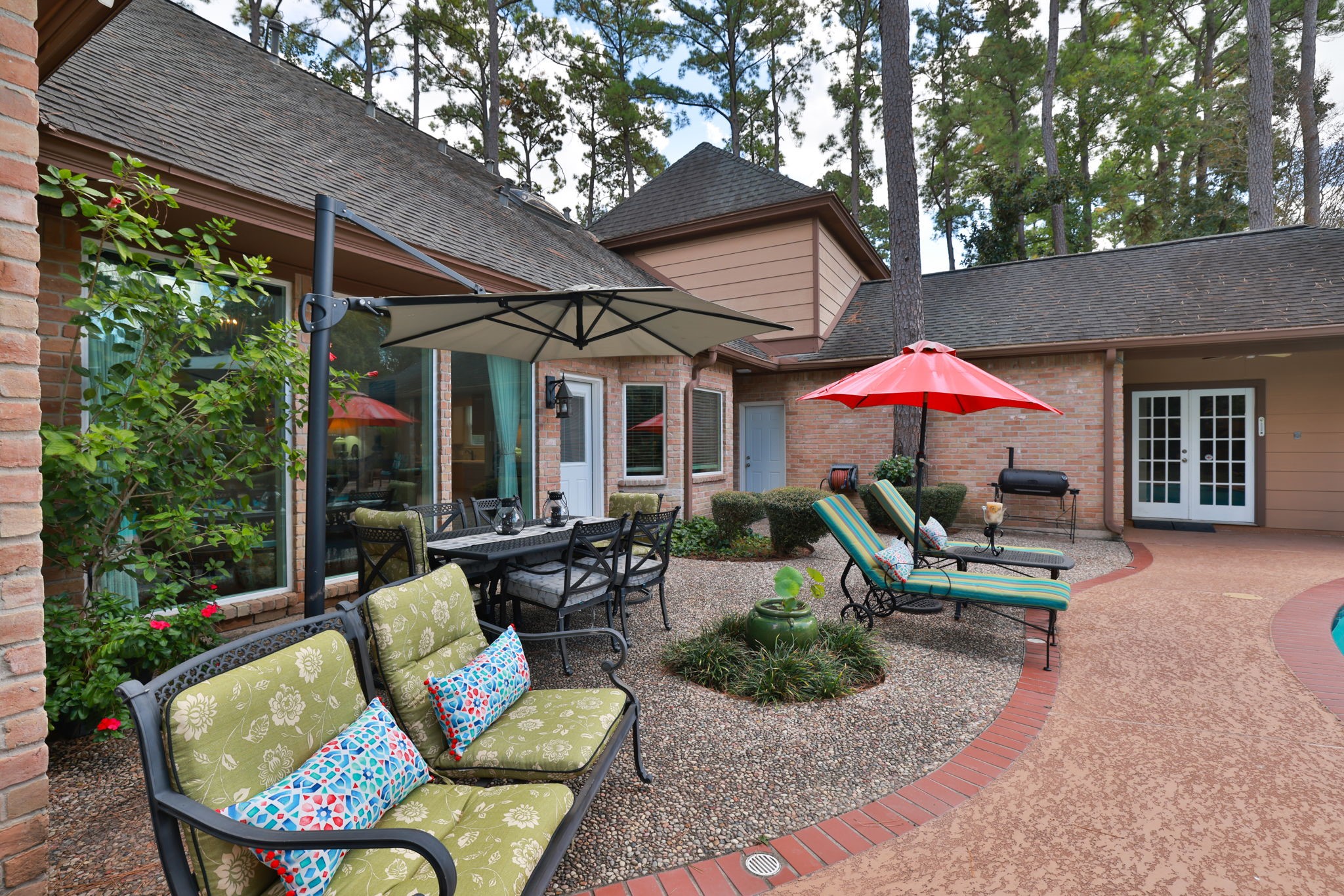 16123 Chasemore Drive Spring, TX 77379 - Photo 45 of 50 The patio features comfortable seating, a dining area with large umbrellas for shade, and lush greenery. The space is perfect for relaxing or entertaining, with direct access to the home and surrounded by tall trees for added privacy.