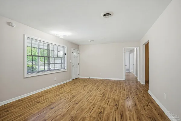 a view of an empty room with wooden floor and a window