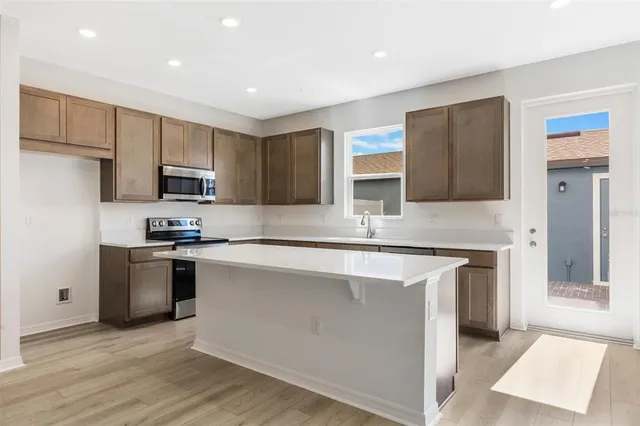 a kitchen with kitchen island granite countertop a stove top oven a sink dishwasher and a refrigerator with wooden floor