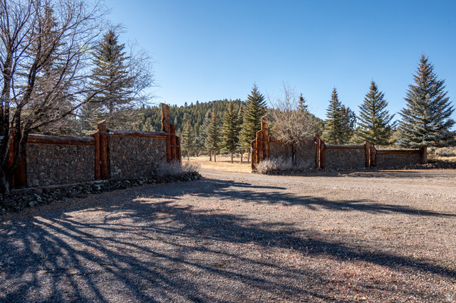 1955 West Mammoth Crk Road Hatch, UT 84735 - Photo 3 of 52 Stone and wood-finish entry wall with a gravel driveway, surrounded by mature evergreen trees