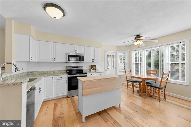 a kitchen with stainless steel appliances granite countertop a stove top oven a sink dishwasher and white cabinets with wooden floor