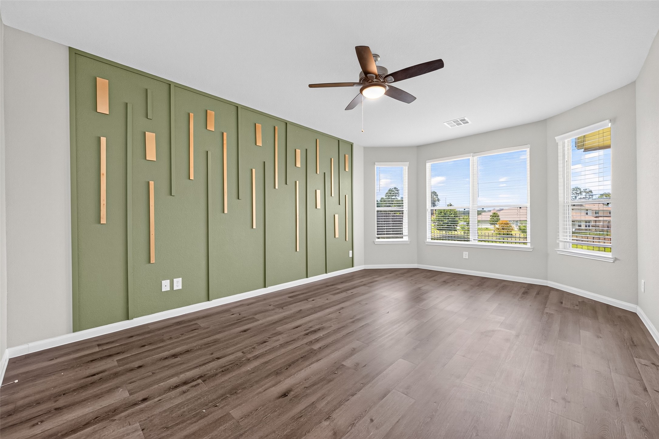 2526 Sturgeon Way Conroe, TX 77384 - Photo 19 of 49 Bright, spacious room with modern wood flooring and a stylish green accent wall featuring vertical panel designs. Large windows offer ample natural light and a scenic view. Ceiling fan included.