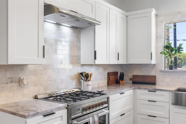 a kitchen with granite countertop a stove a sink dishwasher and white cabinets with wooden floor