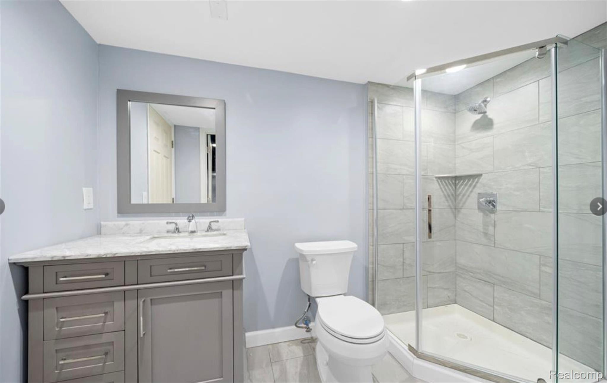 4214 Berkshire Road Royal Oak, MI 48073 - Photo 16 of 27 Bathroom featuring a corner vanity with a stone countertop, a framed mirror, a toilet, a glass-enclosed shower, and large format wall tiling