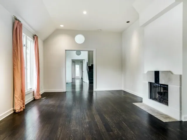 an empty room with wooden floor fireplace and windows