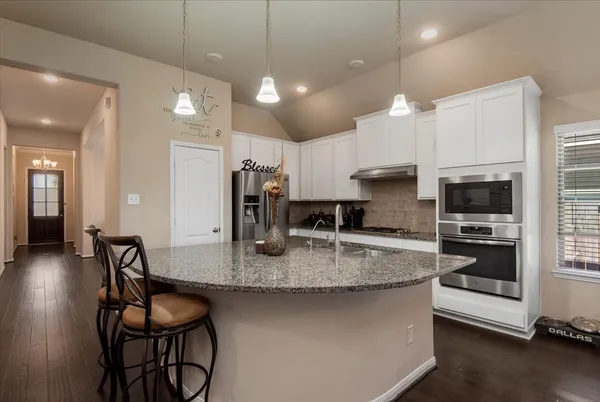 a kitchen with stainless steel appliances granite countertop a stove a refrigerator a sink a dining table and chairs with wooden floor