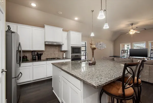 a kitchen with stainless steel appliances granite countertop a stove top oven a refrigerator a sink and chairs