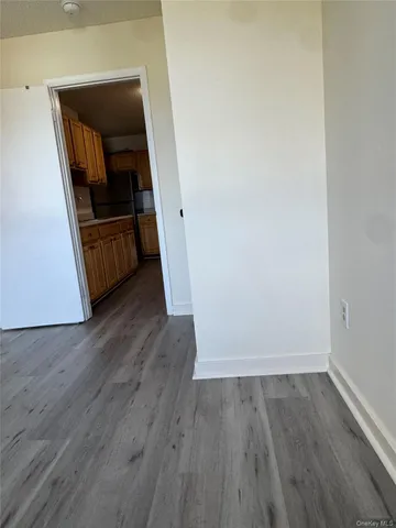 an empty room with wooden floor and way to kitchen