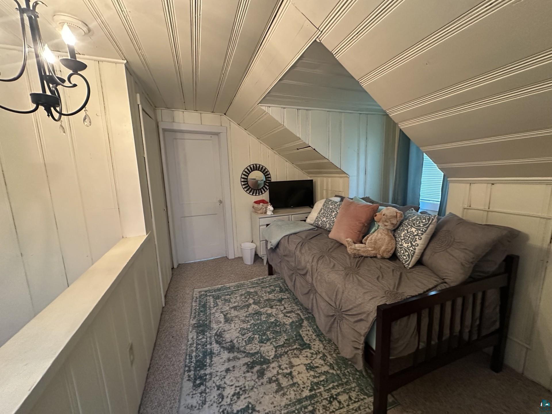 208 Chestnut Street Cloquet, MN 55720 - Photo 20 of 24 Attic space with sloped paneled ceilings and walls, recessed door, and a black wrought iron chandelier