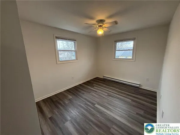 a view of an empty room with wooden floor and chandelier fan