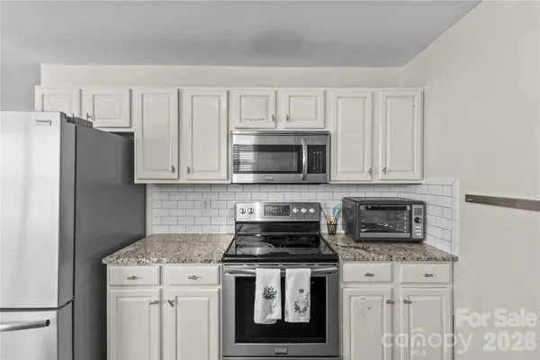 a kitchen with stainless steel appliances granite countertop white cabinets a stove a microwave and a refrigerator