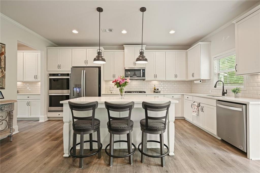 6915 Rambling Vale Dawsonville, GA 30534 - Photo 20 of 63 a kitchen with stainless steel appliances kitchen island granite countertop a wooden floor and white cabinets