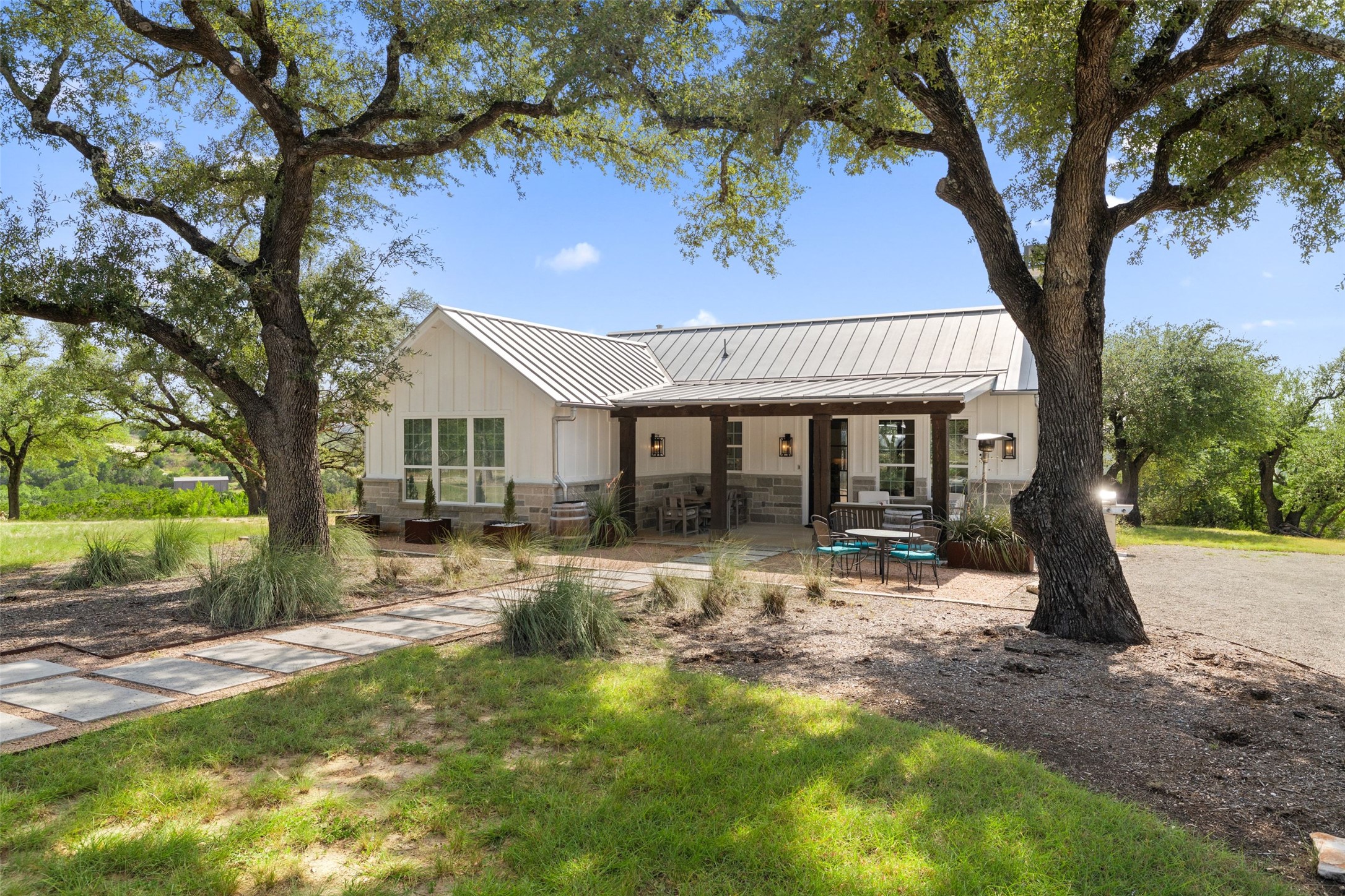 810 Kothmann Road Dripping Springs, TX 78620 - Photo 5 of 40 Mature trees frame a modern farmhouse featuring a metal roof and native stone accents.