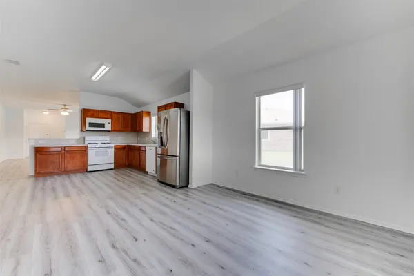 an empty room with wooden floor kitchen view and a window