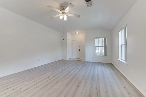 an empty room with wooden floor ceiling fan and window