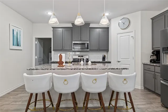 a kitchen with stainless steel appliances granite countertop a stove a refrigerator a kitchen island a sink cabinets and chairs