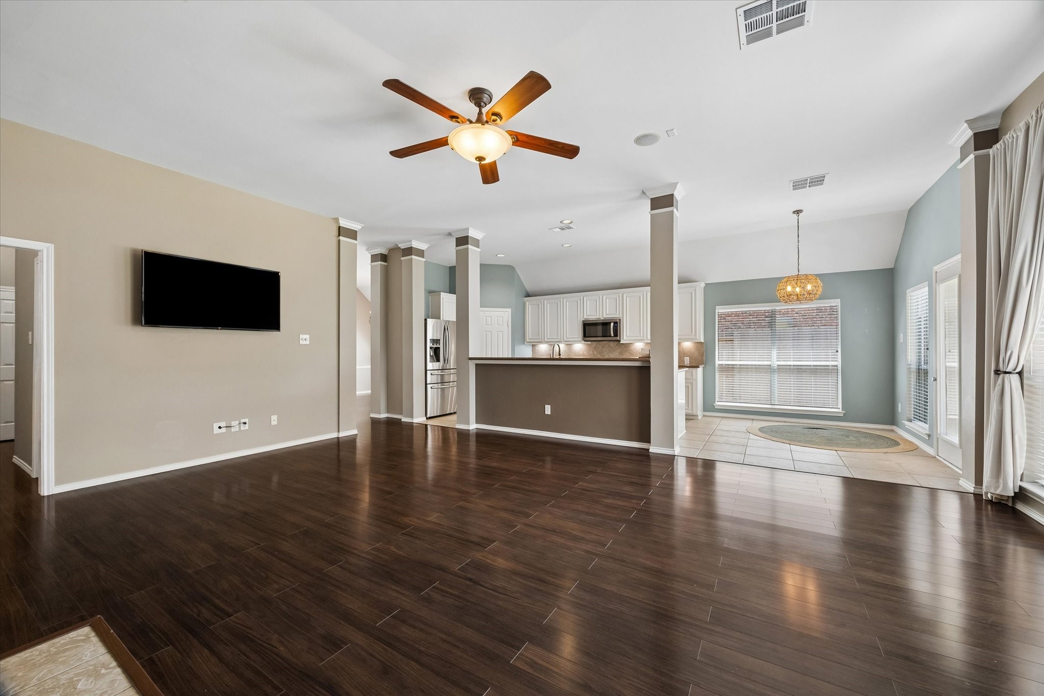 3118 Valley Court Manvel, TX 77578 - Photo 26 of 38 This open-concept living space features rich wood flooring, a ceiling fan, and modern lighting. The kitchen boasts stainless steel appliances, white cabinetry, and a breakfast bar. Adjacent is a dining area with large windows and tiled flooring, offering ample natural light.
