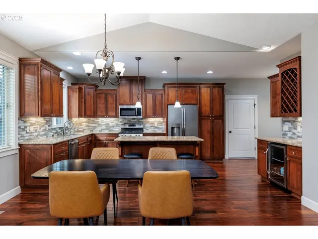 a kitchen with stainless steel appliances kitchen island granite countertop a dining table chairs and a refrigerator