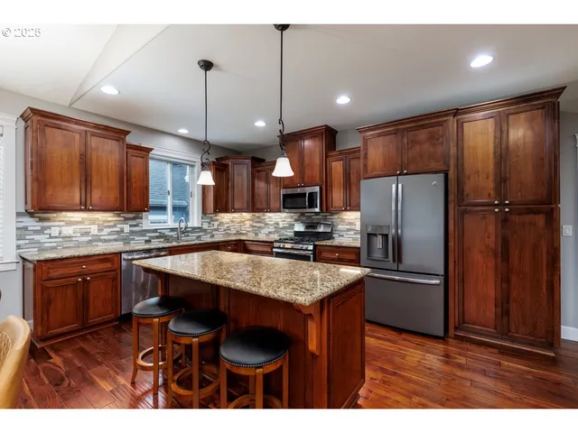 a kitchen with stainless steel appliances granite countertop a refrigerator a sink dishwasher a stove with wooden cabinets and floor