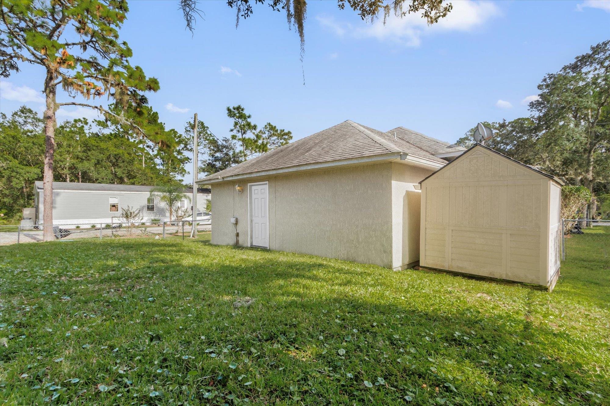 3372 4th Street Elkton, FL 32033 - Photo 28 of 36 View of side of property with stucco siding, a storage shed, and roof with shingles