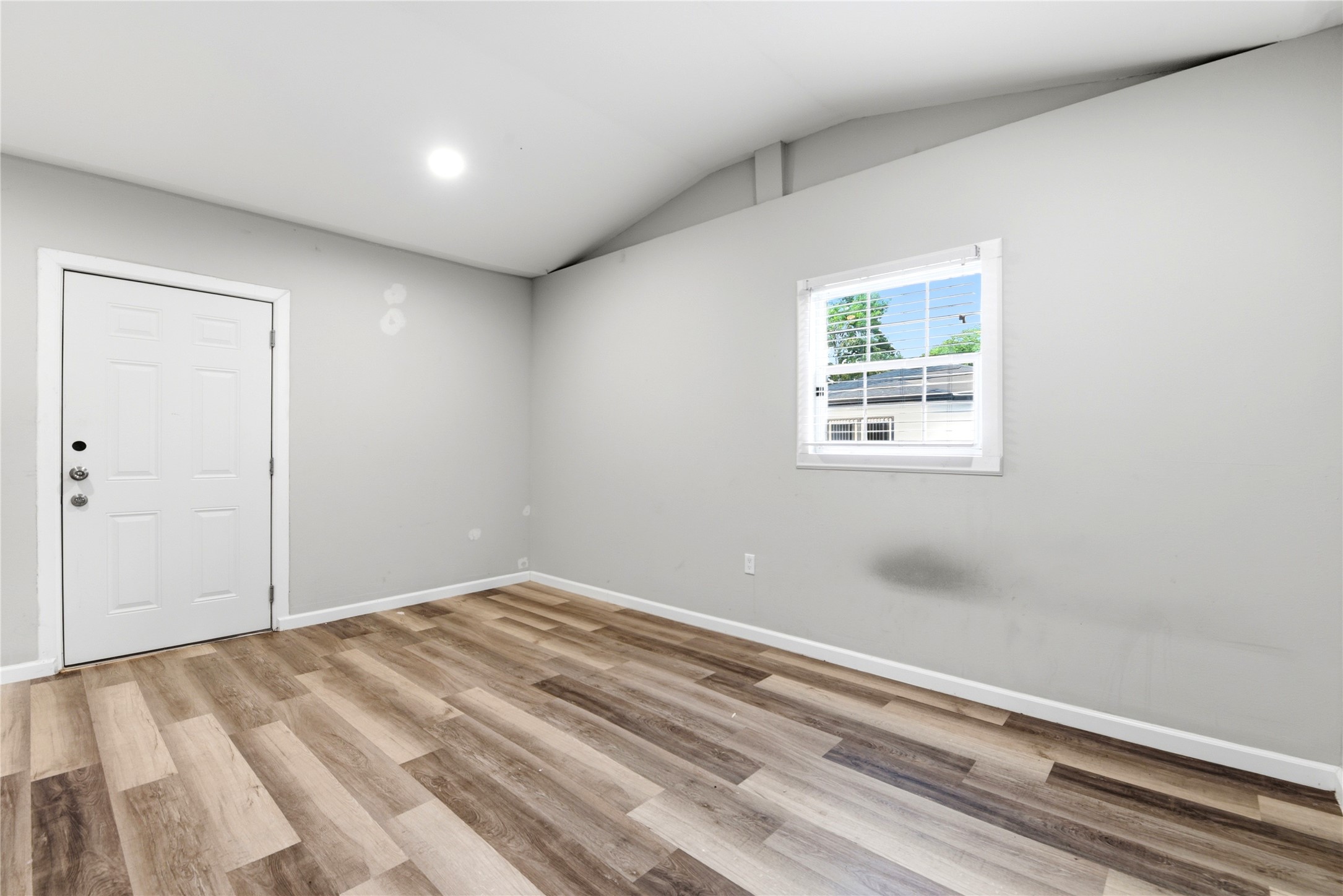 9403 Spaulding Street Houston, TX 77016 - Photo 40 of 50 This room features a simple, modern design with light gray walls, a high ceiling, and wood-look flooring. It has a window providing natural light and a white door, offering a clean, versatile space.